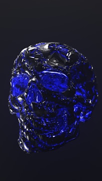 A crystalline skull crafted from a deep blue material, reflecting light on its facets. The intricate details of the crystal create a sense of elegance and mystique against a dark background.