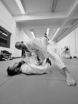 High-resolution image of two athletes engaged in a controlled jiu-jitsu sparring session on a minimalist white mat.