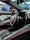 The interior of a modern car featuring a sleek black steering wheel with red stitching, advanced dashboard, and luxurious leather seats. The design is contemporary with high-tech elements and attention to detail.