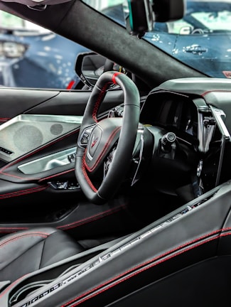 The interior of a modern car featuring a sleek black steering wheel with red stitching, advanced dashboard, and luxurious leather seats. The design is contemporary with high-tech elements and attention to detail.