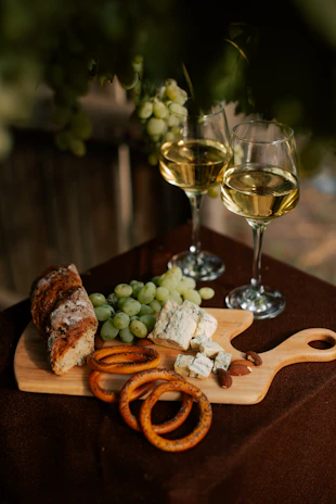 A rustic wooden board with an assortment of artisanal cheeses and fresh grapes beside a glass of red wine.