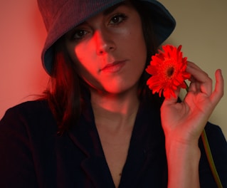 a woman in a hat holding a red flower