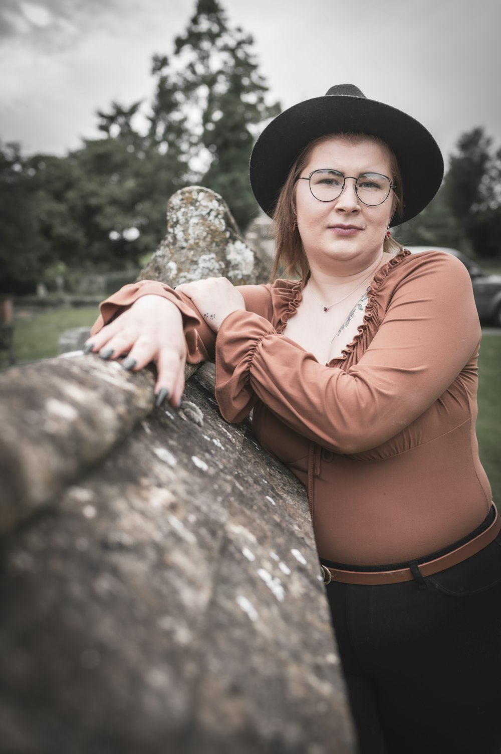 a woman wearing glasses and a hat leaning on a stone wall