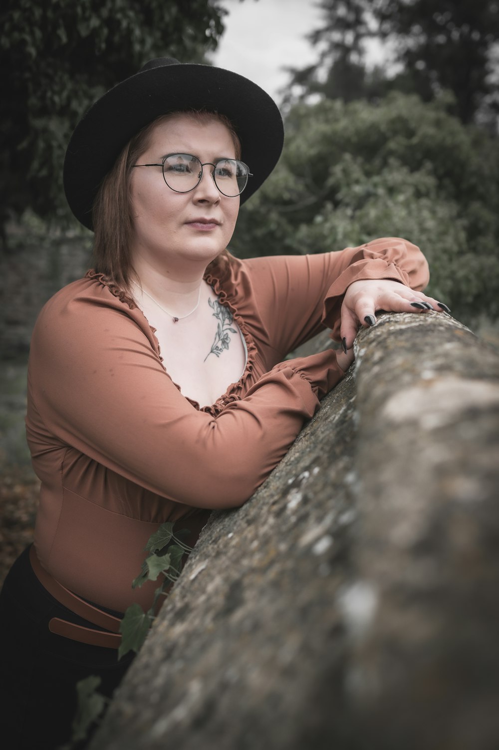 a woman wearing glasses and a hat leaning on a rock