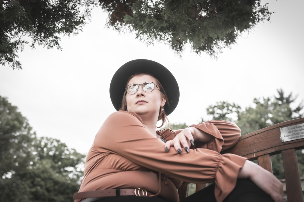 a woman wearing a hat and glasses sitting on a bench