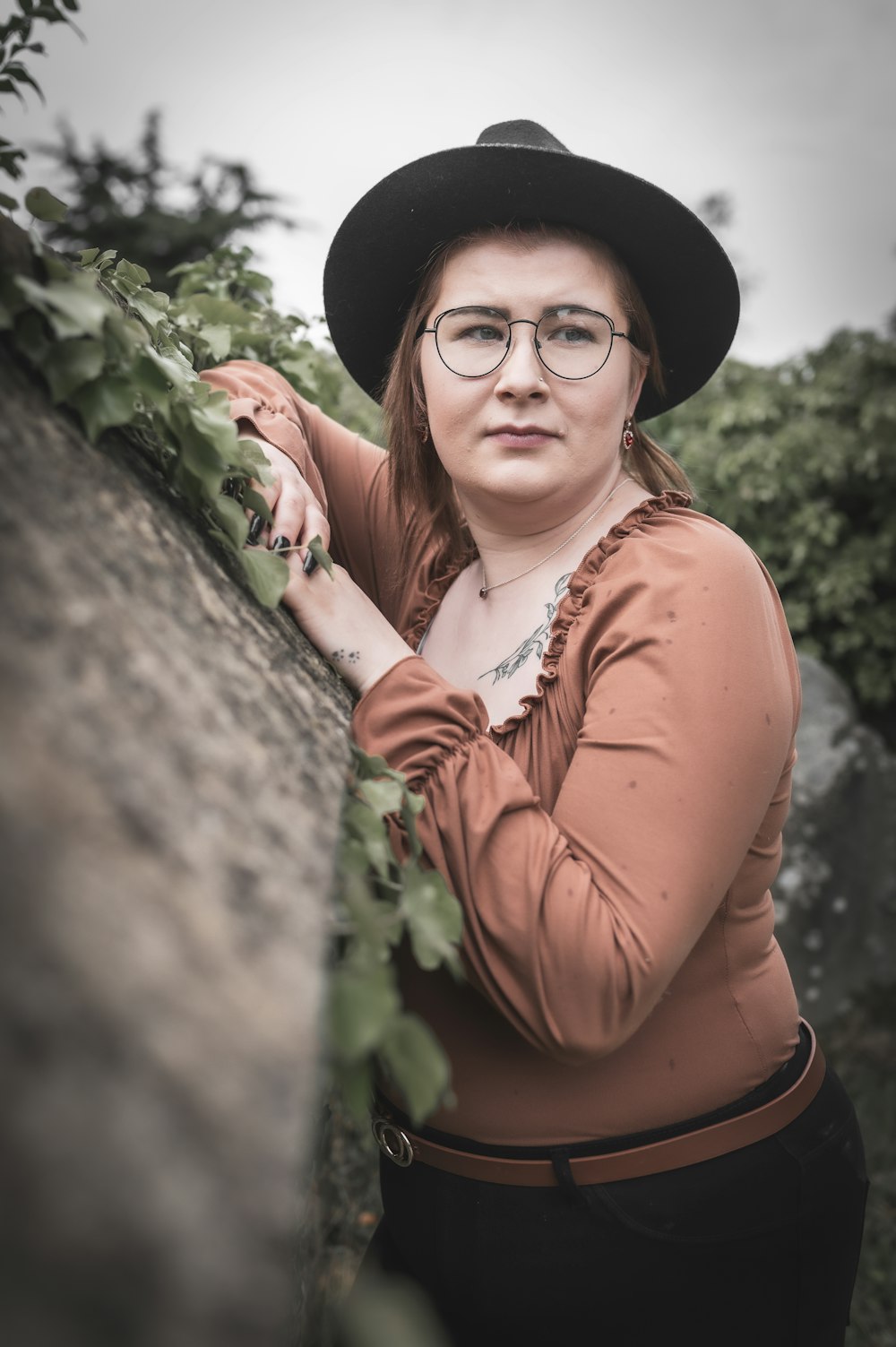 a woman wearing glasses and a hat leaning against a wall