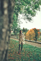 A serene outdoor scene with a model wearing a flowing trench coat, surrounded by falling leaves.