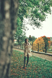 Seasonal outfit with a soft beige trench coat and matching boots framed by autumn leaves.