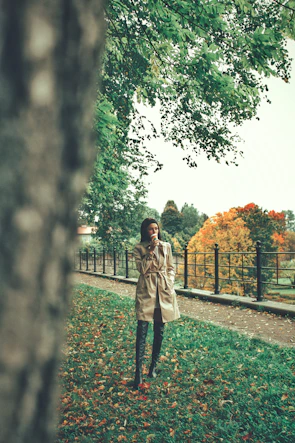 A model wearing a chic trench coat walking through a leafy autumn park