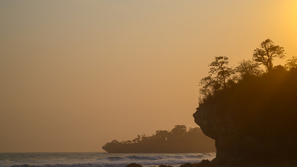 the sun is setting over the ocean with a rock outcropping