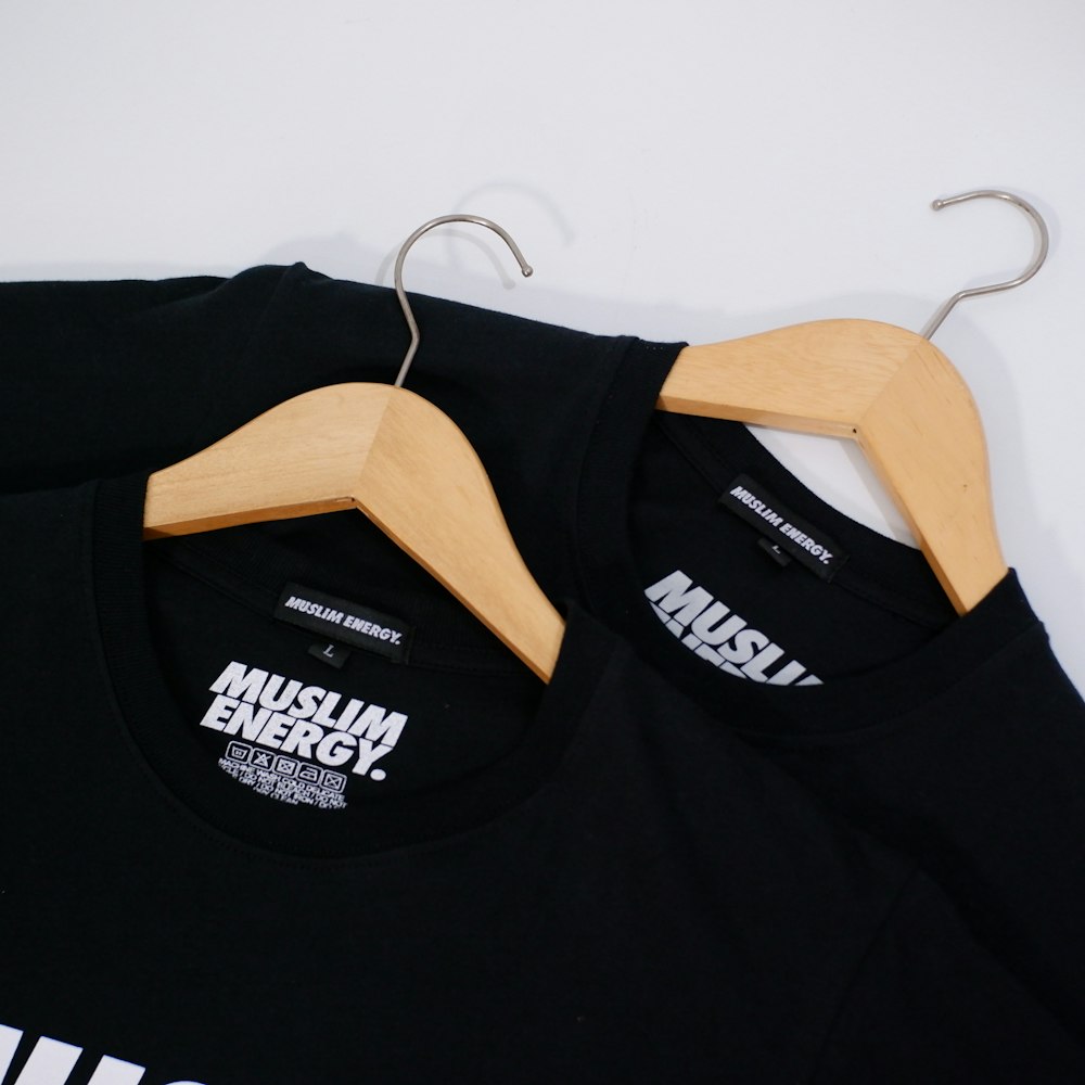 a pair of black t - shirts hanging on a wooden hanger