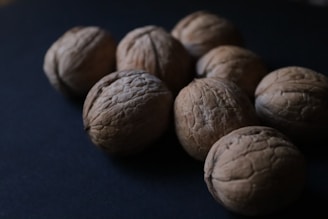 A group of walnuts on a dark surface, displaying their textured, rough shells and natural brown color.