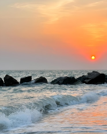 Waves crashing softly against rocks with a backdrop of a pastel sunset sky.