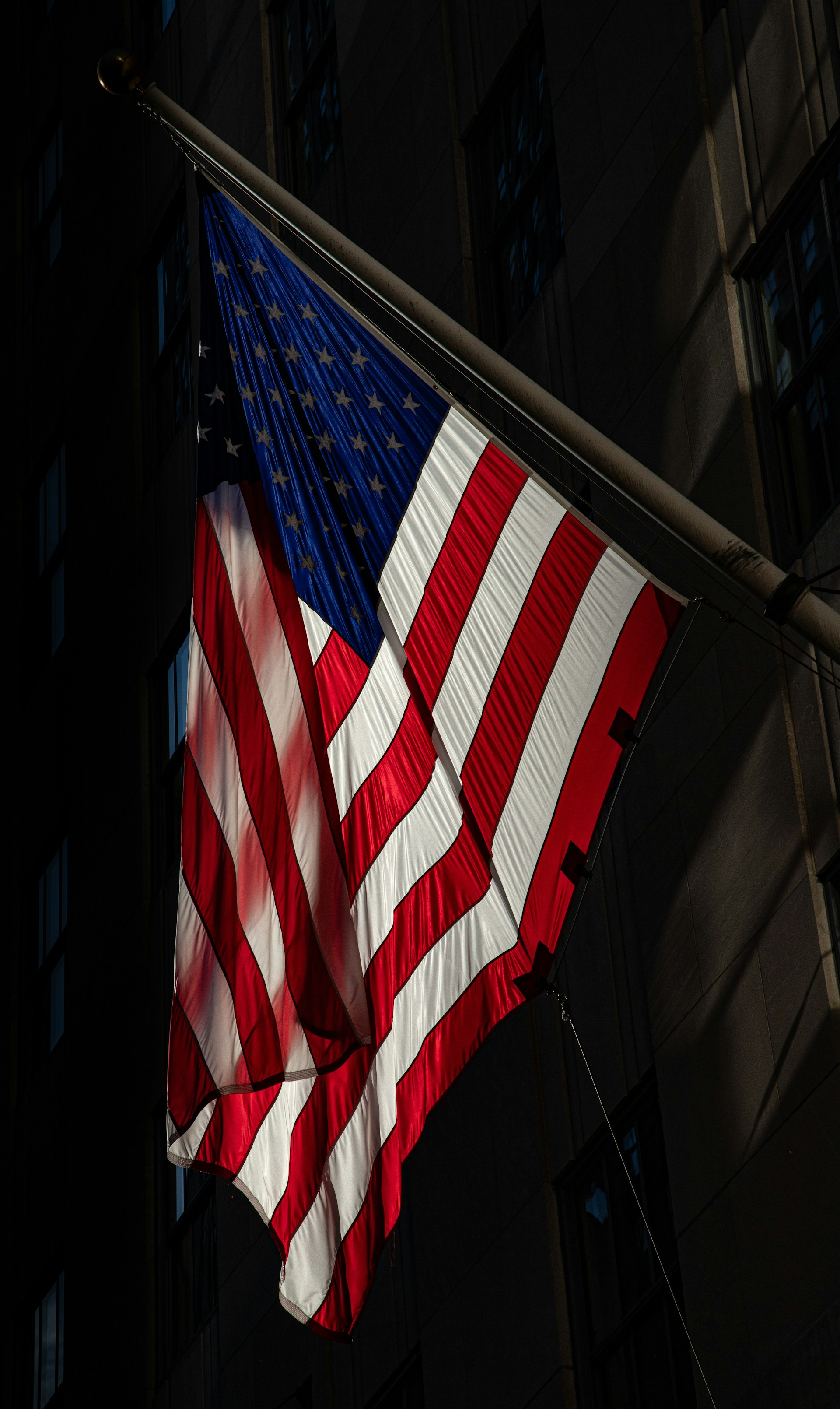 two american flags flying in the wind in front of a building