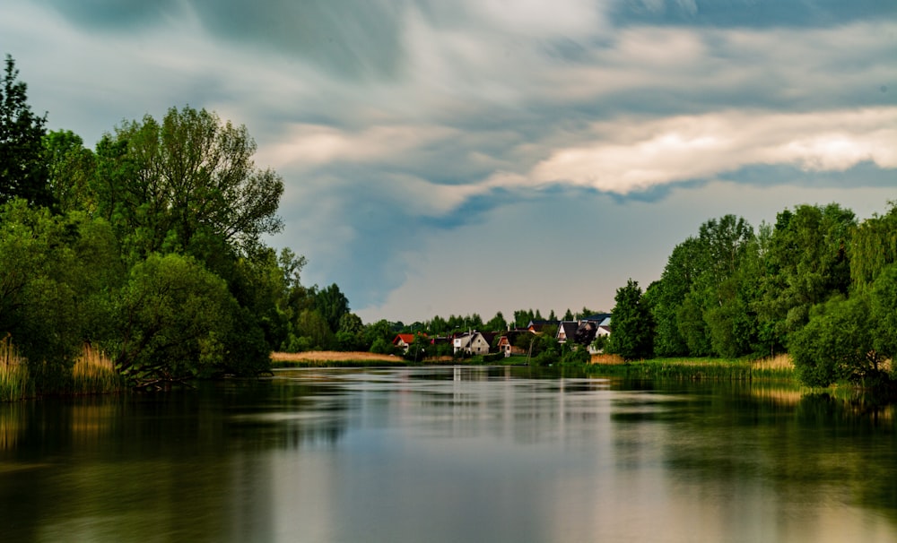 a body of water surrounded by trees under a cloudy sky