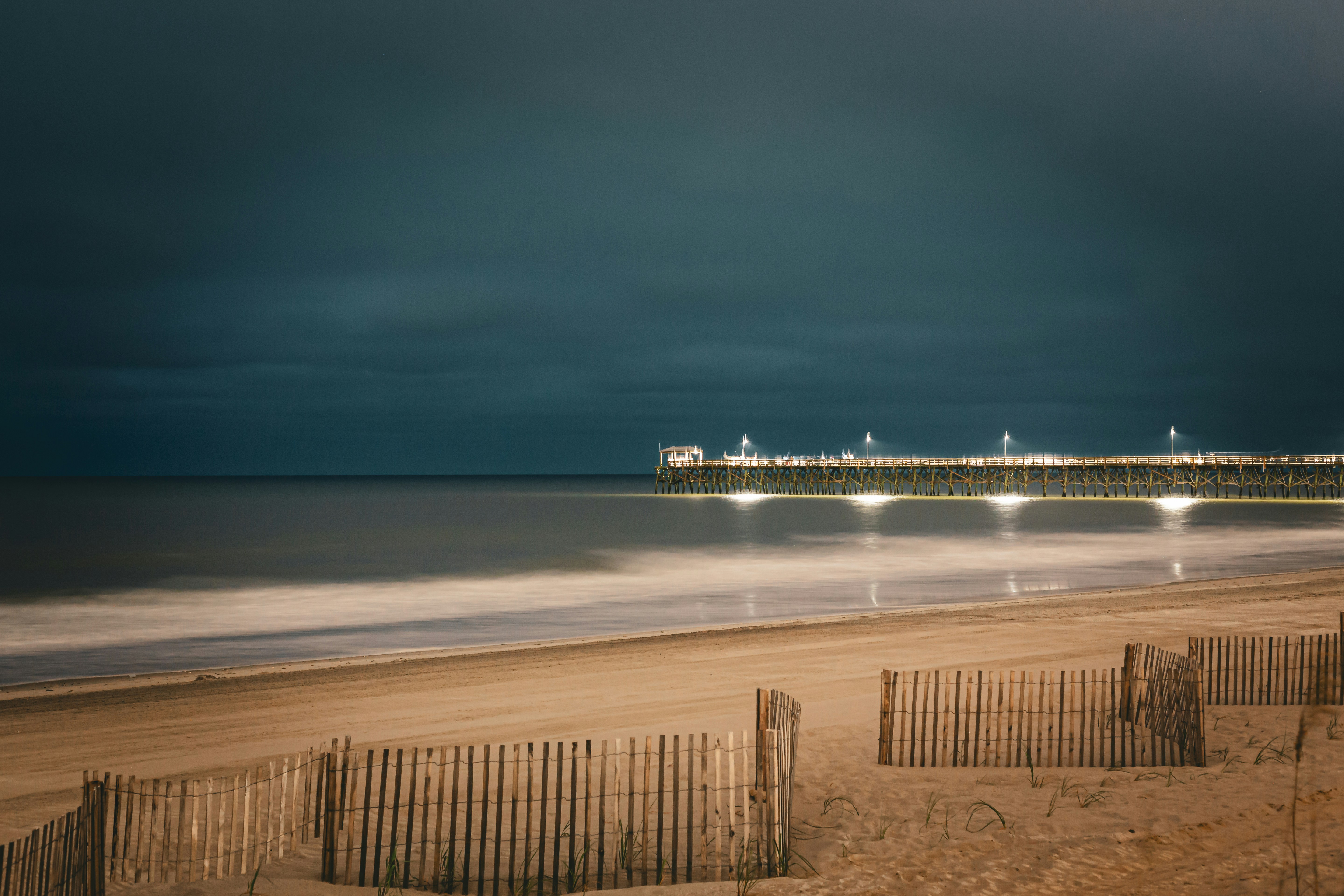A beach with a pier in the distance under a cloudy sky photo – Free ...