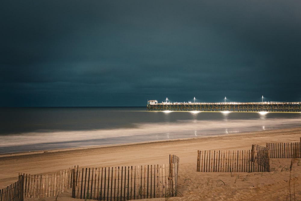 a beach with a pier in the distance under a cloudy sky