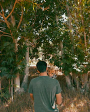 A volunteer gently holding a rescued dog in a sunlit garden surrounded by greenery.