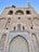 A large, ancient brick structure with tall arches and intricate tile work featuring blue patterns. The facade is detailed, showcasing historical architecture with several windows and an arched entry that is partially blocked. The building seems to be undergoing restoration work.