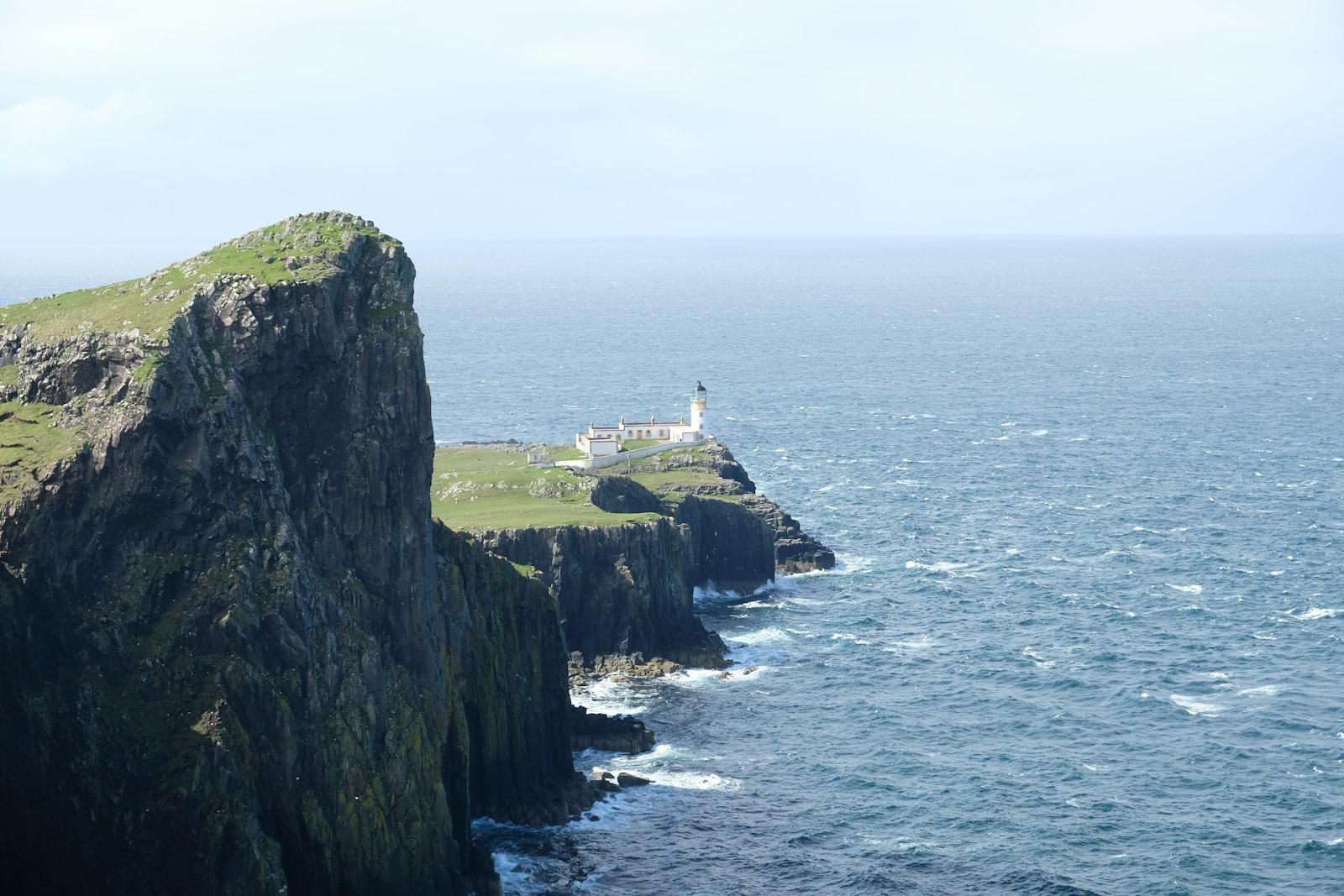 A lighthouse standing on rugged sea cliffs with waves breaking on the rocks far below