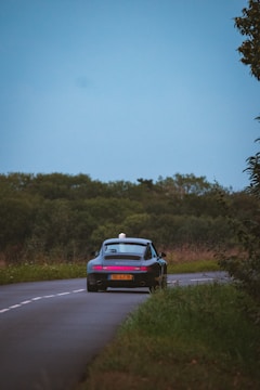A vintage convertible cruising down a scenic country road under a clear blue sky.
