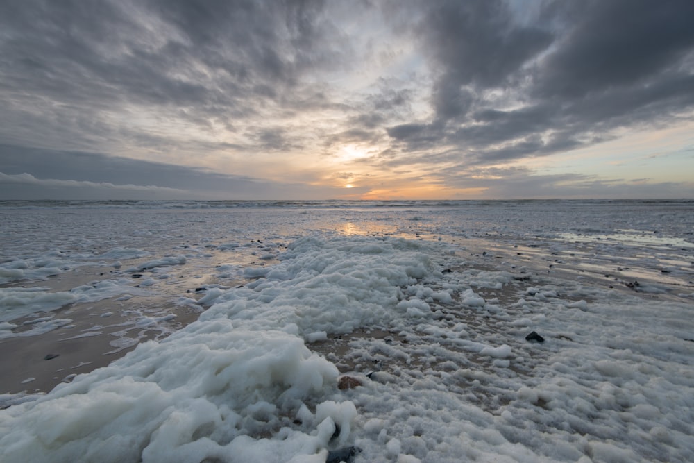 a beach covered in ice and water under a cloudy sky