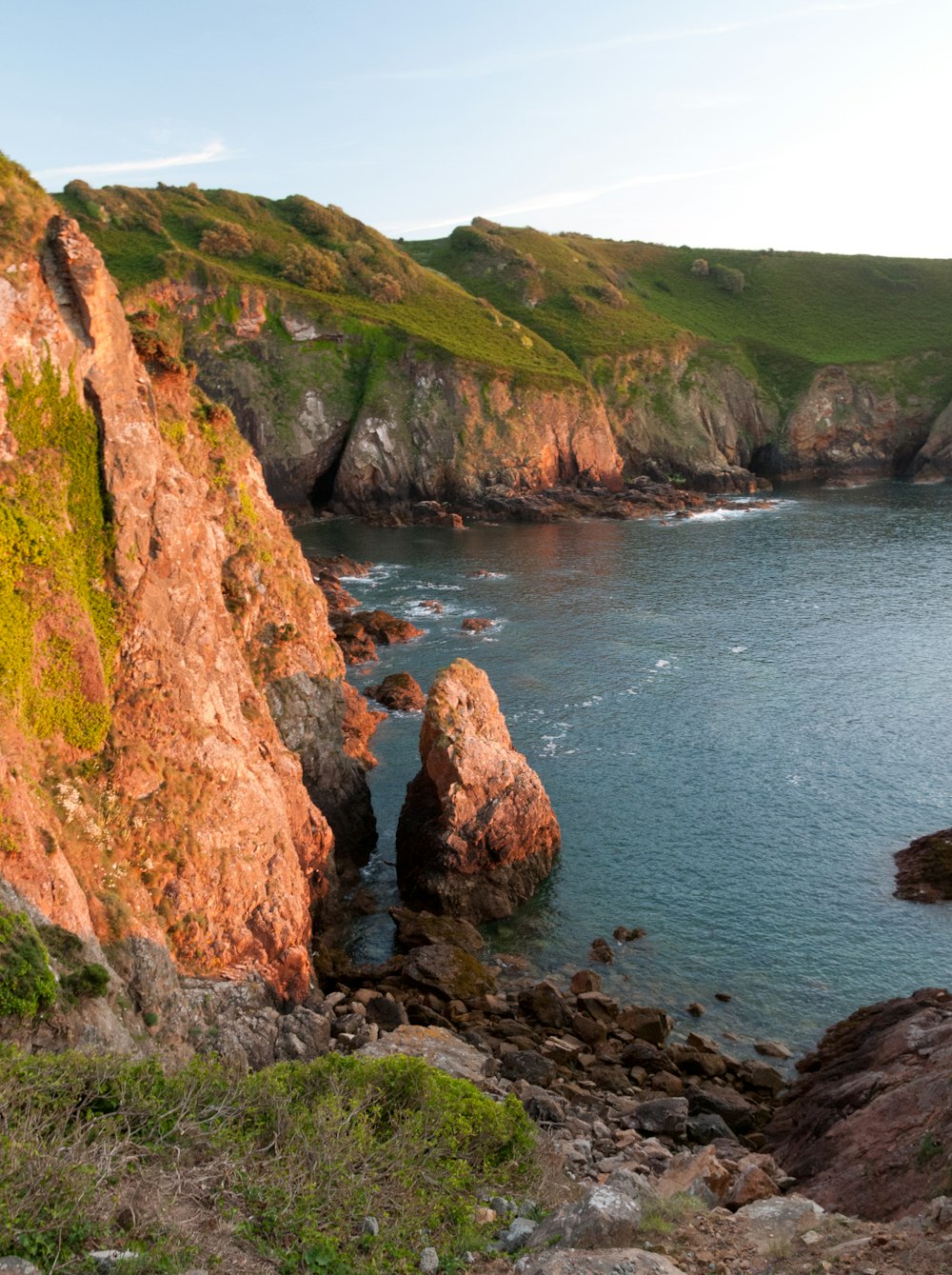 a large body of water next to a lush green hillside