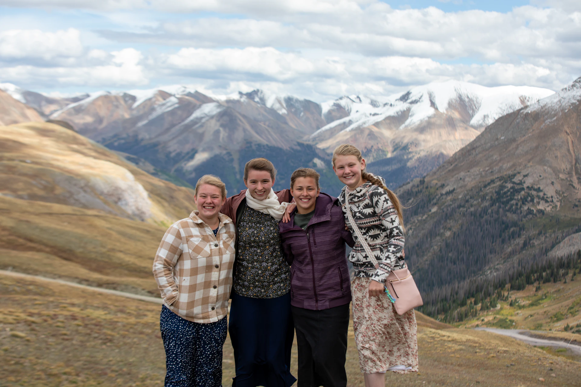 A joyful group of friends wearing colorful Altessa ponchos and sweatshirts, sharing a moment outdoors in a lush mountain setting.