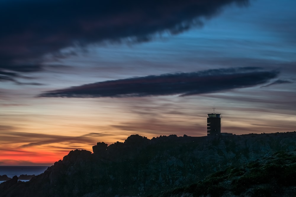 a lighthouse on top of a hill with a sunset in the background