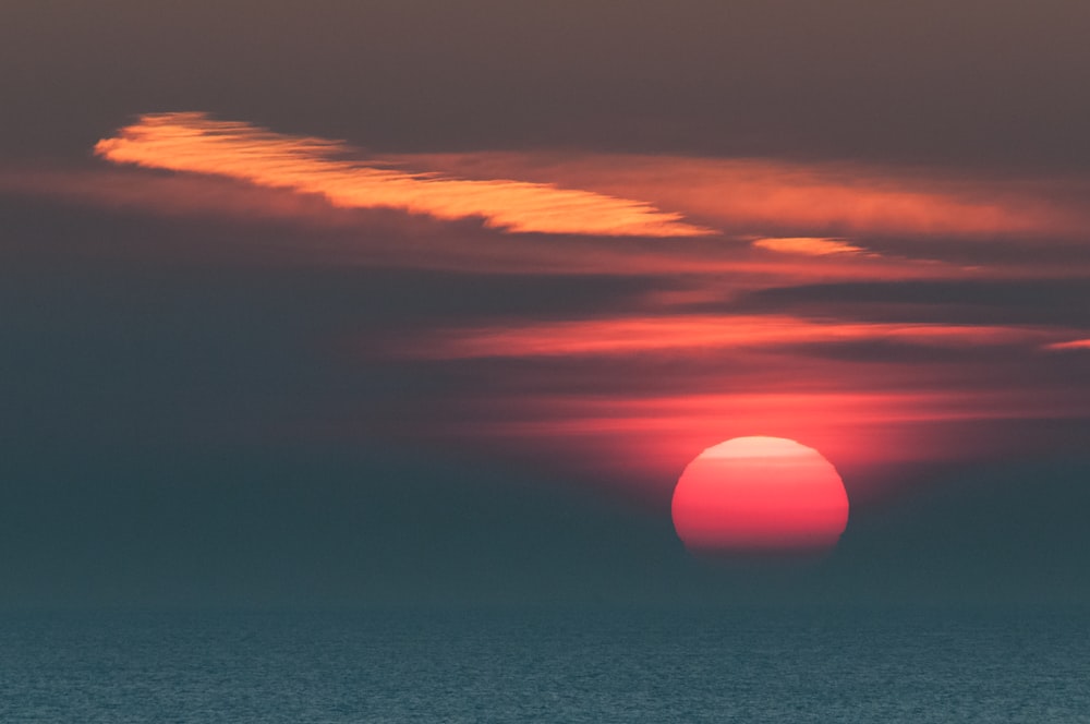 the sun is setting over the ocean on a cloudy day