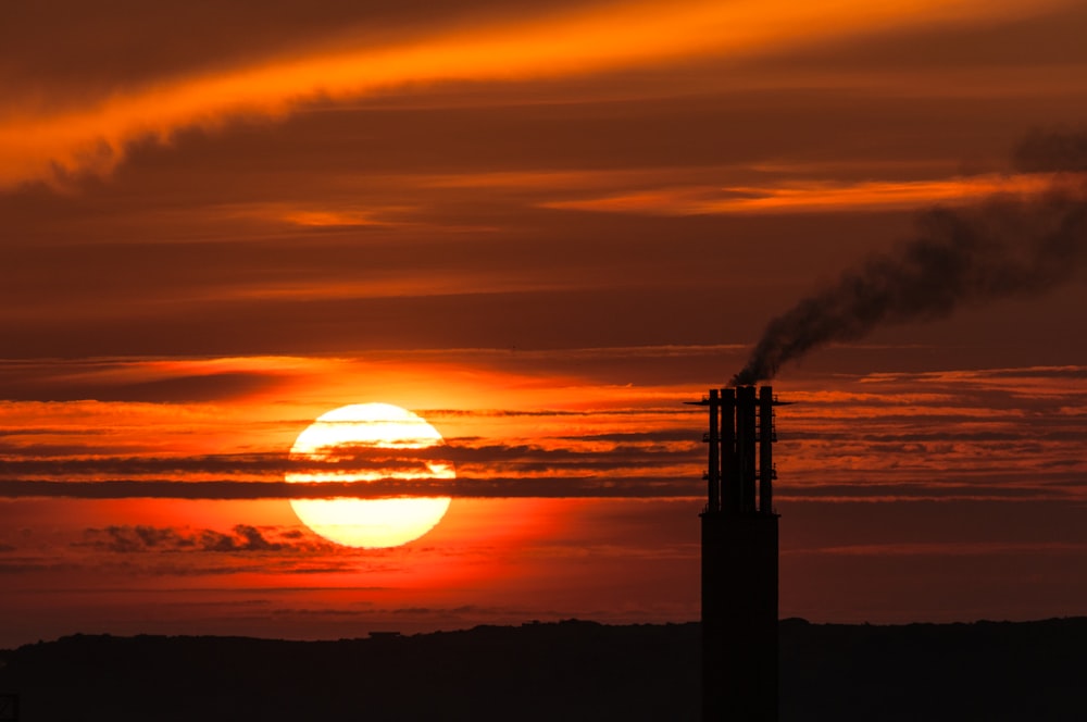 the sun is setting behind a smoke stack