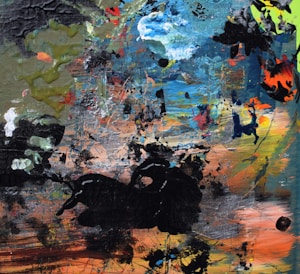 An abstract painting featuring a chaotic blend of textures and colors. Brush strokes and splatters in shades of blue, green, orange, and black create a dynamic and energetic composition. The surface is filled with layers of paint, creating a sense of depth and complexity.