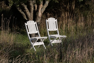 a couple of white chairs sitting next to each other in a field