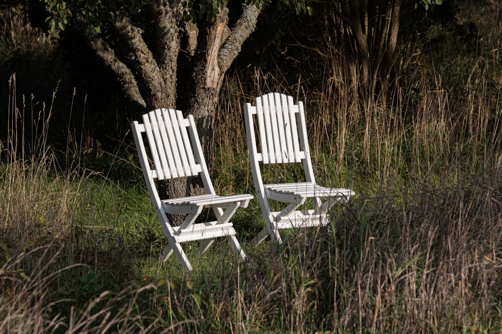 a couple of white chairs sitting next to each other in a field