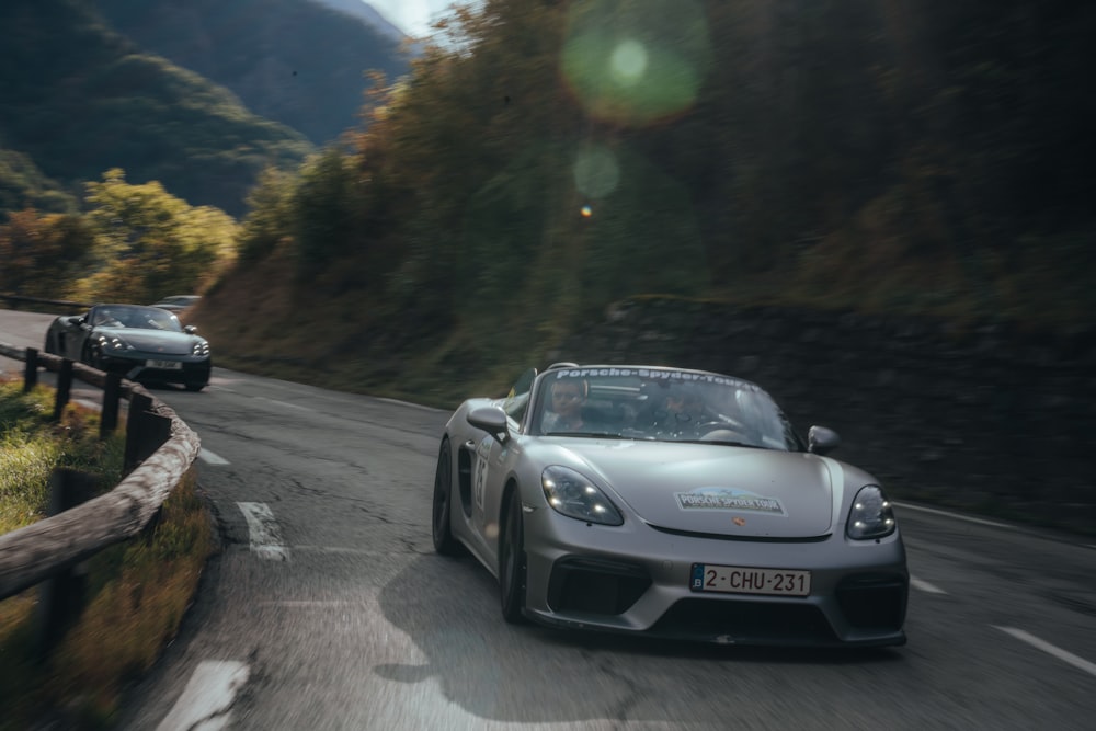 a silver sports car driving down a mountain road