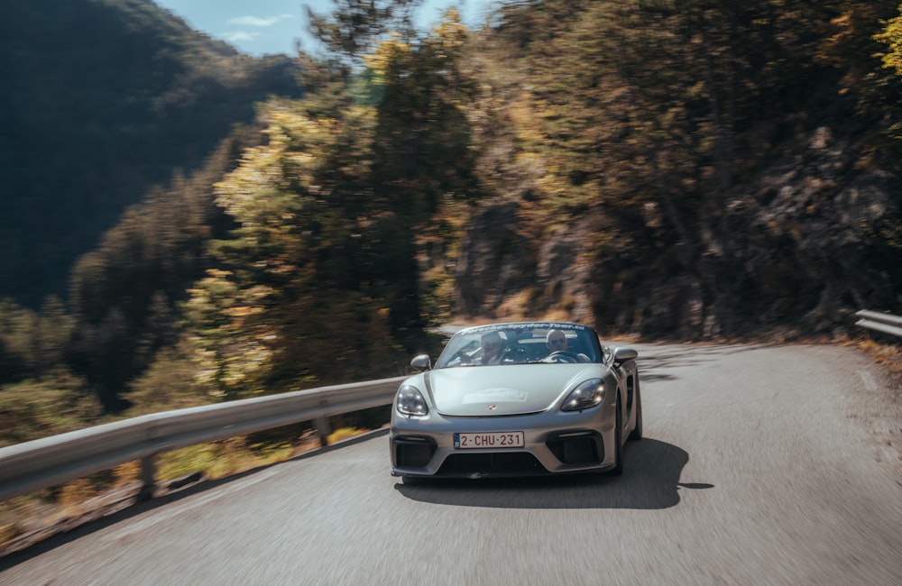 a silver sports car driving down a mountain road