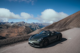 A shiny black convertible cruising along a coastal highway under a clear blue sky.
