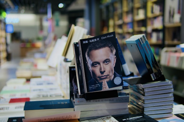 A display of books in a bookstore with a prominent book featuring a person's face on the cover. The setting is well-lit with shelves filled with books in the background, creating a cozy bookstore atmosphere.