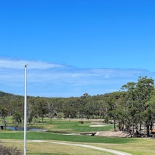 A panoramic view of a golf course beside a calm river under a clear sky.