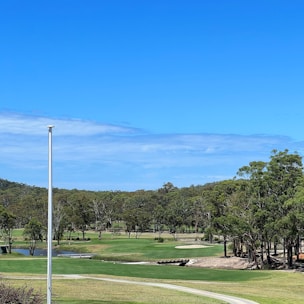 A panoramic view of a golf course beside a calm river under a clear sky.