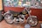 A vintage Norton 850 Commando motorcycle is displayed on a tiled floor. The motorcycle has a black body with polished chrome detailing and a classic design. Behind it, there is a wall covered with various automotive-related posters and photographs.