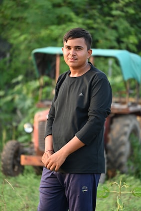 Portrait of Raj Kumar Boora standing confidently in front of fertile farmland near Bhiwani under a clear sky.