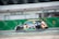 A racing car is speeding on a track, featuring a black body with colorful decals, including logos and the number 45. The background is blurred, indicating fast motion. Sponsorships from various brands are visible on the car's body.