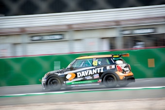 A racing car is speeding on a track, featuring a black body with colorful decals, including logos and the number 45. The background is blurred, indicating fast motion. Sponsorships from various brands are visible on the car's body.