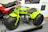 A bright green three-wheeled all-terrain vehicle with large, thick tires is prominently displayed next to a red and black CB125T motorcycle. The green vehicle features a compact engine and is stationed on a platform, surrounded by informational panels discussing motorcycle history.