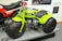 A bright green three-wheeled all-terrain vehicle with large, thick tires is prominently displayed next to a red and black CB125T motorcycle. The green vehicle features a compact engine and is stationed on a platform, surrounded by informational panels discussing motorcycle history.