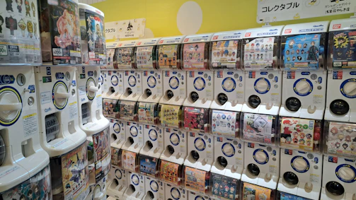 A close-up of a colorful capsule toy dispenser installed in a bright supermarket aisle.