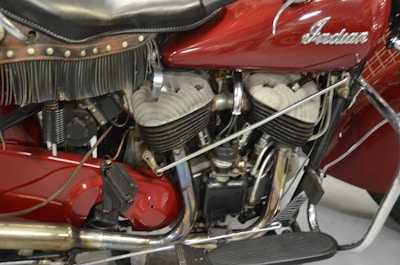 A close-up view of a vintage motorcycle engine with intricate mechanical details and a leather seat with fringe. The surface of the engine parts is metallic and slightly worn, suggesting age and use.