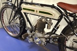 A close-up view of a vintage motorcycle showcasing its detailed engine components, a leather seat, and a distinctive fuel tank design with decorative trim. The motorcycle appears well-maintained, highlighting its intricate mechanical parts and classic styling.