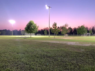 Wide shot of an open grassy field with people setting up for a soccer game at dawn